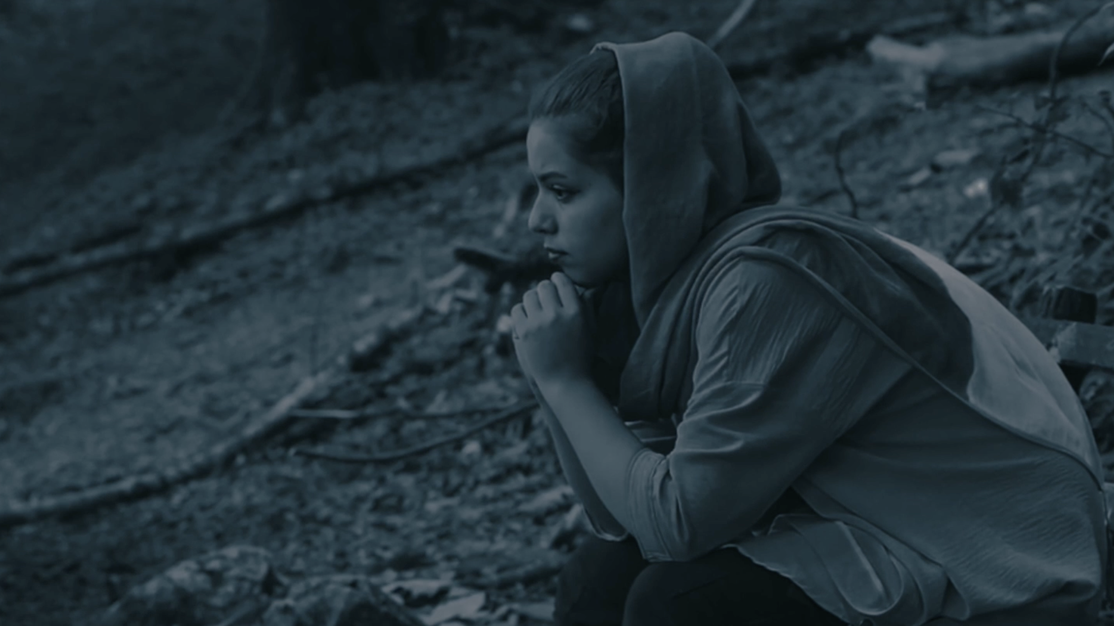 A woman featured in Journey of Hope sits in a wooded landscape